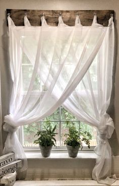 the window is decorated with white curtains and potted plants