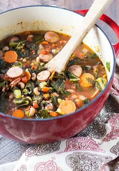 a red pot filled with soup on top of a table next to a wooden spoon