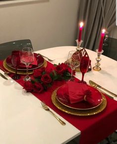 the table is set with red roses and gold place settings for two people to sit at