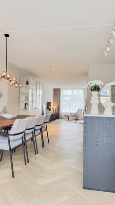 a dining room table and chairs in front of a large mirror with lights hanging from the ceiling