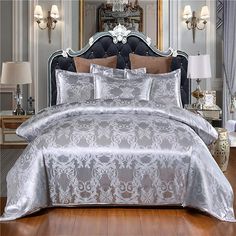 the bed is made up with silver sheets and comforters on top of wooden flooring