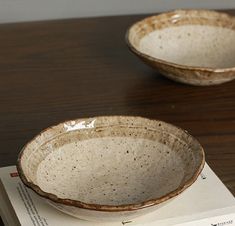 two brown and white bowls sitting on top of a table next to an open book