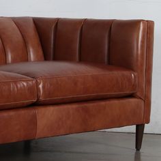 a brown leather couch sitting on top of a hard wood floor next to a white wall