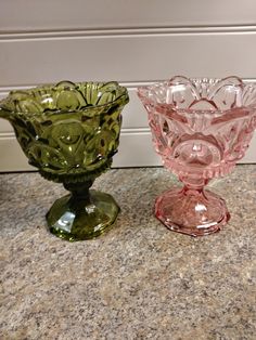 two glass vases sitting on top of a marble countertop next to each other