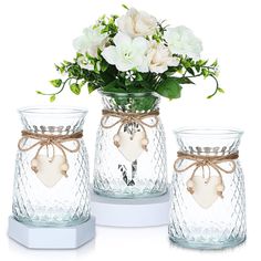 three glass vases with flowers in them on a white tablecloth and two are decorated with hearts