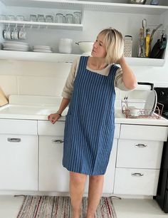 a woman standing in front of a kitchen counter with dishes on the shelves behind her