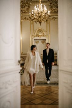 a bride and groom walking through an ornate hallway in front of a chandelier