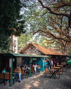 many people are sitting at tables under the trees