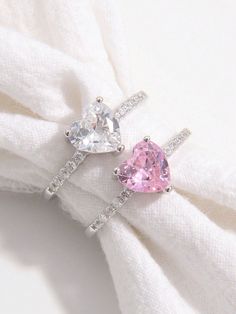 two heart shaped pink and white diamond rings on top of a napkin with a white cloth