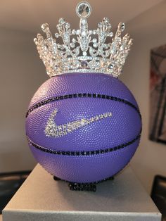 a purple basketball with a crown on top of it sitting on a pedestal in front of a wall