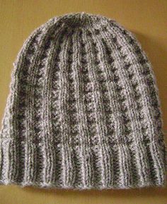 a gray and white knitted beanie sitting on top of a wooden table next to a yellow wall