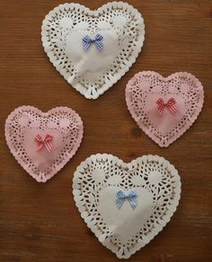 four heart shaped doily with bows on them sitting on top of a wooden table