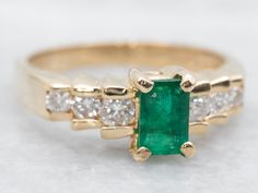 an emerald and diamond ring on a white surface