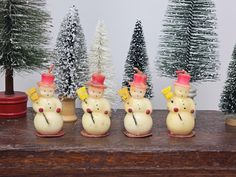 five small snowmen with hats on their heads are lined up in front of christmas trees