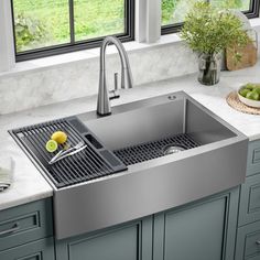 a stainless steel sink in a kitchen with marble counter tops and gray cabinets, along with green plants