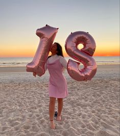 a woman standing on top of a sandy beach next to the ocean holding an inflatable number