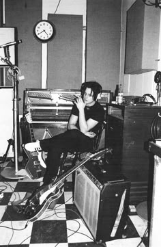 a man sitting on top of a guitar in a room with guitars and other musical equipment