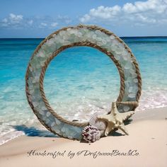 a wreath made out of seashells is on the sand near the ocean shore