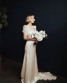 a woman in a white dress holding flowers and looking off to the side with her hand on her hip