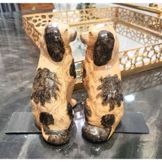 two ceramic dogs sitting next to each other on top of a black table with gold trimming