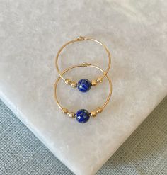 Vibrant blue lapis lazuli stones hung on delicate gold filled hoops. Lapis lazuli is known as the stone of friendship. They are super easy to put in and comfortable to wear all day. Each hoop measures 15mm in diameter and they are available in gold filled or sterling silver. Each pair comes beautifully gift wrapped. Lapis Lazuli is one of the most sought after stones in use since man's history began. Its deep, celestial blue remains the symbol of royalty and honour, gods and power, spirit and vision. It is a universal symbol of wisdom and truth. Gold filled is made by heat and pressure bonding a layer of karat gold to a metal core. Unlike gold plated, gold filled has an actual layer of karat gold, not just a microscopic film and with the proper care will last a lifetime. I am committed to Blue Hoop Brass Jewelry, Blue Brass Hoop Jewelry, Blue Gold-plated Hoop Earrings, Dainty Blue Hypoallergenic Hoop Earrings, Blue Dainty Hypoallergenic Hoop Earrings, Dainty Blue Hoop Jewelry, Dainty Blue Hoop Earrings, Blue Gold Plated Hoop Jewelry, Blue Dainty Hoop Jewelry