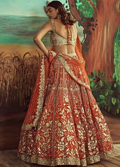 Features an orange lehenga in luxurious organza embellished with leather applique and highlighted with mirrorwork and rose gold sequins work. Teamed with a contrasting gold blouse and a matching orange and gold net dupatta embroidered with buttis and a gold border. Composition: Lehenga- Organza, Blouse-Organza, Dupatta-Net Care: Dry Clean Only and Vacuum Storage This product can be customised for sleeves, length of blouse and neckline Delivery : 6-8 weeks as the product is hand crafted. For more