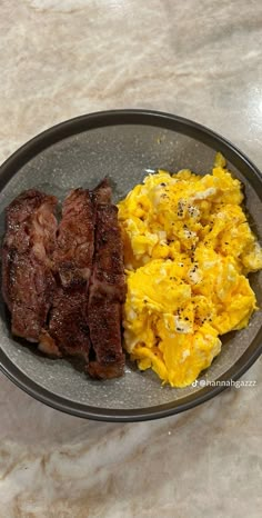 two pieces of meat and scrambled eggs in a bowl on a marble counter top with a spoon