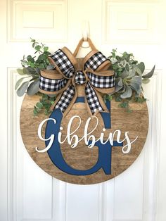 a door hanger with the letter g on it that says gibbings and is decorated with greenery