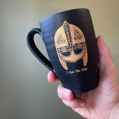 a hand holding a black coffee mug with an image of a helmet on it