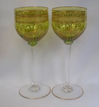 two wine glasses sitting next to each other on a white tableclothed surface, one is green and the other is yellow