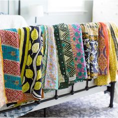 a row of colorful scarves hanging from a metal rack on a bed in a bedroom