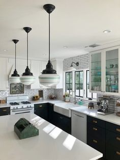 a kitchen with white counter tops and black pendant lights hanging from the ceiling over the island