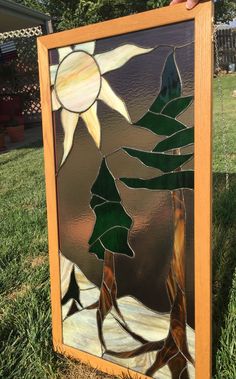 a hand holding up a stained glass window with trees and sun in the sky on it