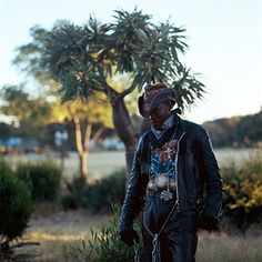 a man standing next to a tree in the middle of a field with grass and bushes