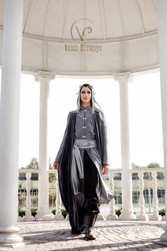 a woman standing in front of a white gazebo wearing black and grey clothing with long veil on her head