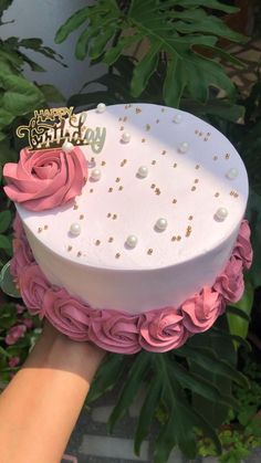 a birthday cake decorated with pink roses and gold dots is being held by someone's hand