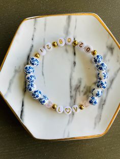 a blue and white beaded bracelet with gold accents on a marble plate, sitting on a table