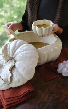 a woman holding a spoon over a bowl filled with soup next to garlic cloves