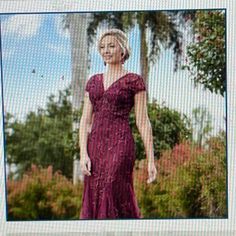 a woman in a long purple dress is posing for a photo with trees and bushes behind her