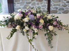 flowers are arranged on the back of a white tablecloth draped by a stone wall