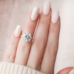 a woman's hand with a white manicured nail polish holding a diamond ring