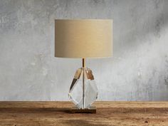 a clear glass table lamp sitting on top of a wooden table next to a wall