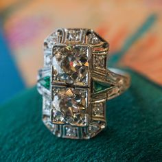 ANTIQUE DOUBLE DIAMOND & EMERALD COCKTAIL RING IN PLATINUM This Antique Double Diamond & Emerald Cocktail Ring in Platinum is what dreams are made of! This one of a kind Art Deco ring features two (2) old European cut diamonds, accent emeralds, and .30 total carats of diamond accents in platinum. With a striking look, the twin old European cut diamonds glitter at the center of a boxy milgrain mounting design. Detailed and utterly attractive, the emerald accents  bring a touch of color the the sp Art Deco Multi-stone Platinum Diamond Ring, Platinum Emerald Cut Multi-stone Diamond Ring, Art Deco Multi-stone Diamond Ring, Classic Multi-stone Platinum Diamond Ring, Platinum Multi-stone Diamond Ring For Anniversary, Platinum Multi-stone Emerald Ring In White Gold, Platinum Multi-stone Diamond Wedding Ring, Emerald Cut Multi-stone Platinum Rings, Art Deco Platinum Multi-stone Rings