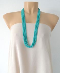 a woman wearing a white top with a turquoise beaded necklace on it's neck