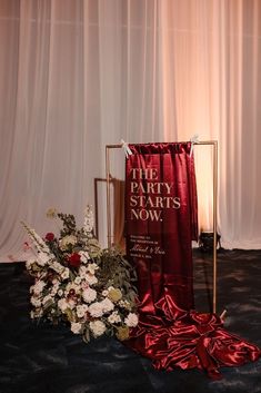 the party starts now sign next to flowers and a red banner on a black carpet