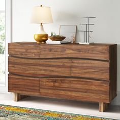 a wooden dresser with a lamp on top of it next to a rug and window