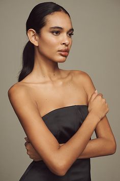 a woman in a strapless dress poses for a studio portrait with her arms crossed