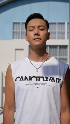 a man with his eyes closed standing in front of a building and wearing a white tank top