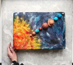 a person is holding their hand near a painting on the wall with planets in it