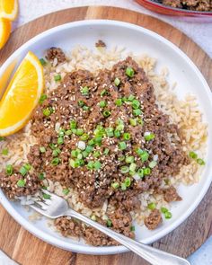 a white plate topped with meat and rice next to an orange wedge on a wooden cutting board